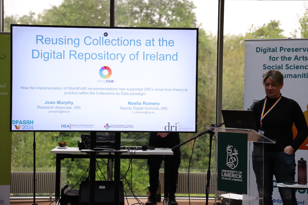 Joan Murphy presenting at the DPASSH conference, standing behind a podium on the right with the screen projecting the presentation to the left.