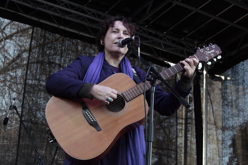 Close-up of Evelyn Campbell on stage with purple scarf and a guitar.