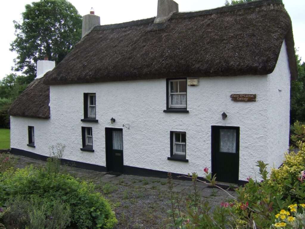 A picturesque white house adorned with a thatched roof, set against a backdrop of lush vegetation and bright skies.